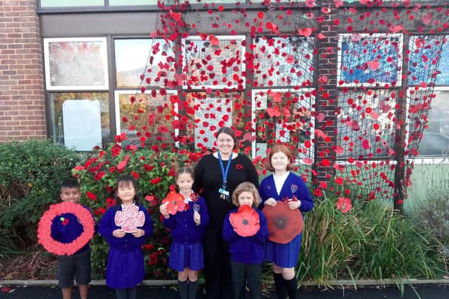 (L to R) Mikail Ghury, 7, Alice Hu, 6, Lydia Scott, 8, Acting Headteacher Izzy Lewis, Griff Harrison-Jones, 5, and Charis Hargreaves alongside a 'poppy wave' of over 1000 poppies.