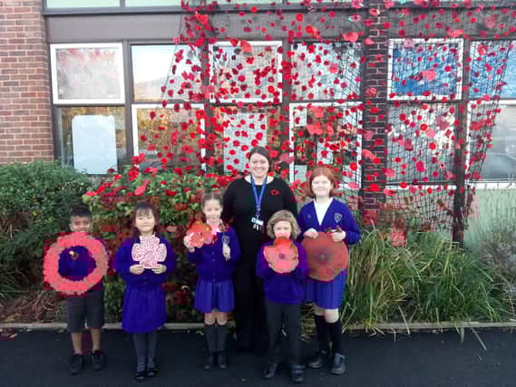 (L to R) Mikail Ghury, 7, Alice Hu, 6, Lydia Scott, 8, Acting Headteacher Izzy Lewis, Griff Harrison-Jones, 5, and Charis Hargreaves alongside a 'poppy wave' of over 1000 poppies.
