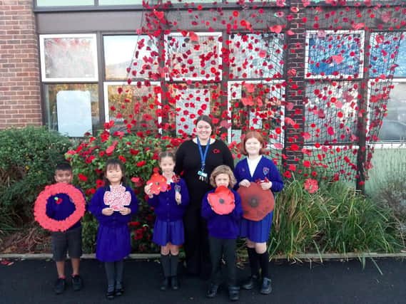(L to R) Mikail Ghury, 7, Alice Hu, 6, Lydia Scott, 8, Acting  Headteacher Izzy Lewis, Griff Harrison-Jones, 5, and Charis Hargreaves alongside a 'poppy wave' of over 1000 poppies.