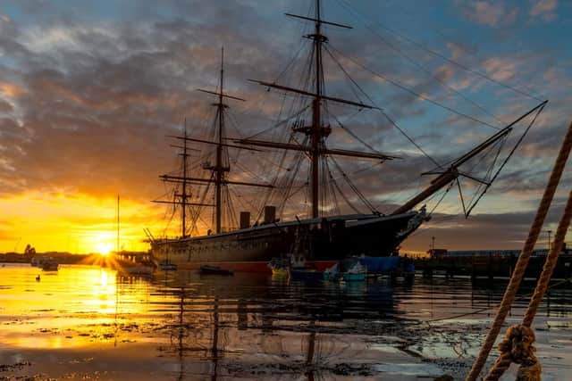 A glowing sun partially illuminates HMS Warrior at Old Portsmouth.