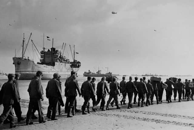 German prisoners of war marching across Normandy beach. Beached cargo vessel behind.