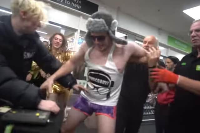 Lee Marshall in a vest and shorts, and wearing a hat, surrounded by Asda staff