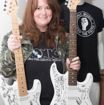 Steph Langan, co-founder of Tonic holds the two autographed guitars that will be auctioned for funds