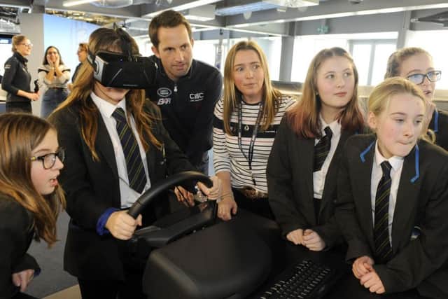 Sir Ben Ainslie helps a pupil take control in a simulation of a multi-hulled America's Cup race boat, watched by her school friends