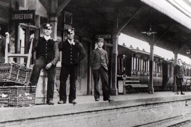 Seen at Hayling Island railway station in 1910 we see three railwaymen very smartly dressed. They all have peaked caps, ties and waistcoats along with carnations in their buttonholes. The man to the left must be the stationmaster and the two porters are dealing with the arrival of pigeons, perhaps to be released outside the station.
To the right is a schoolboy with a smart watch chain attached to his blazer. 
The lad on the far right is wearing a plus-four suit along with an Eton collar.