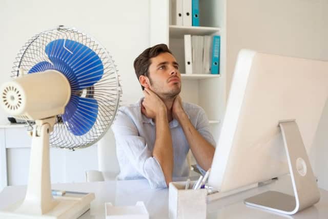 Casual businessman sitting at desk with electric fan in his office