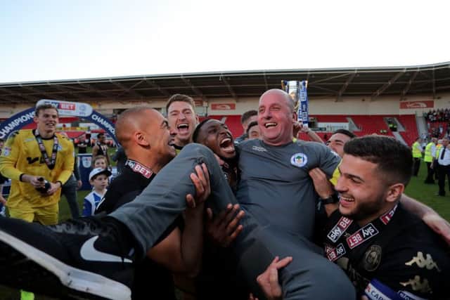 Paul Cook is held aloft by the Wigan players after the Latics clinched the League One title on Saturday