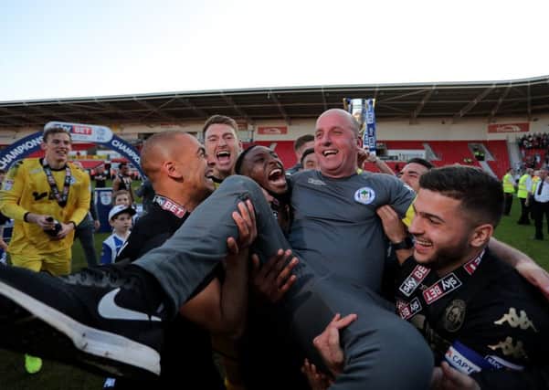 Paul Cook is held aloft by the Wigan players after the Latics clinched the League One title on Saturday