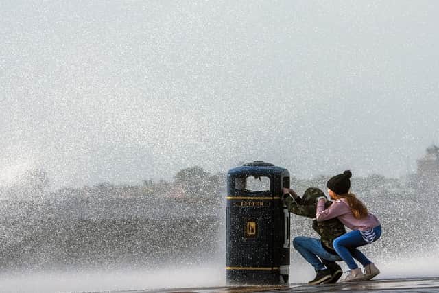 Two children try to keep dry by shielding themselves from one of the many waves that were crashing against the sea wall in Southsea. Picture: Lou Louis