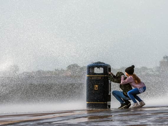 Two children try to keep dry by shielding themselves from one of the many waves that were crashing against the sea wall in Southsea. Picture: Lou Louis