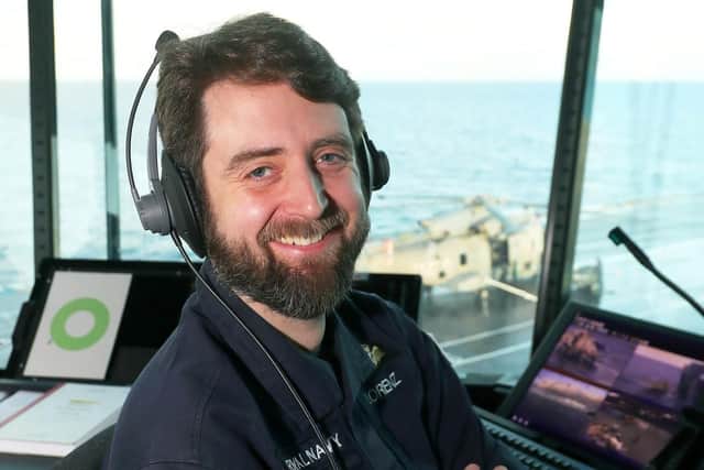 Lt Cdr Lorenz in FLYCO with 820 merlin on deck behind him.