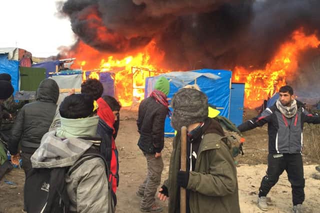 Migrants and activists watch burning makeshift shelters set on fire in the camp near Calais