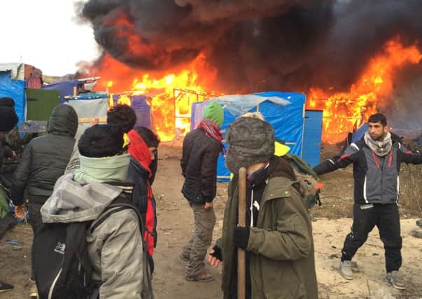 Migrants and activists watch burning makeshift shelters set on fire in the camp near Calais