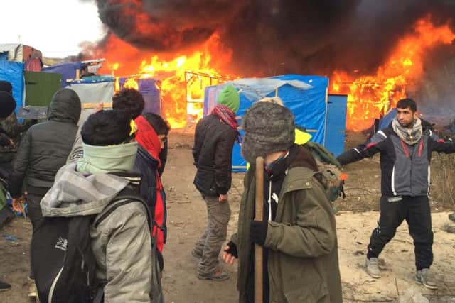 Migrants and activists watch burning makeshift shelters set on fire in the camp near Calais, northern France, (AP Photo/Jerome Delay)