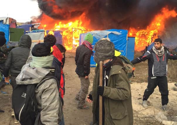 Migrants and activists watch burning makeshift shelters set on fire in the camp near Calais, northern France, (AP Photo/Jerome Delay)