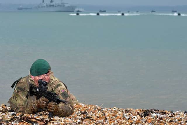 A Royal Marine Commando recces a stretch of beach whilst offshore raiding craft and landing craft carrying troops and vehicles make their approach during a previous exercise at Browndown