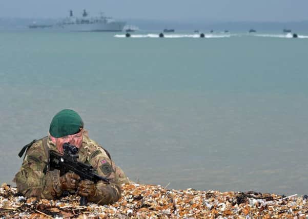 A Royal Marine Commando recces a stretch of beach whilst offshore raiding craft and landing craft carrying troops and vehicles make their approach during a previous exercise at Browndown