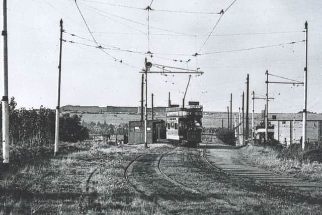 A tram bound for Horndean crosses the bridge over the buses only side road with the bridge over the railway line just ahead of it.