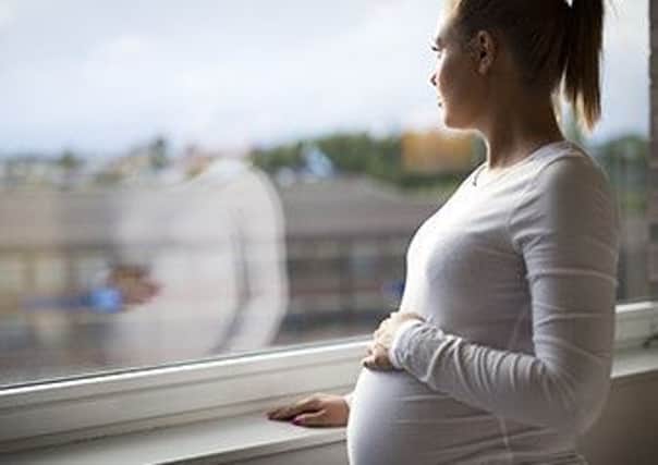 Thoughtful pregnant woman looks out the window home. Holding a hand on the tummy. Mental health and pregnancy.