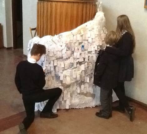 Children add their prayers for others to the sculpture