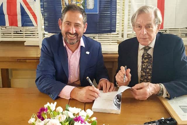 Kevin Porter, left, and Rear Admiral Jeremy Larken, right, sign copies of Kevins book, below