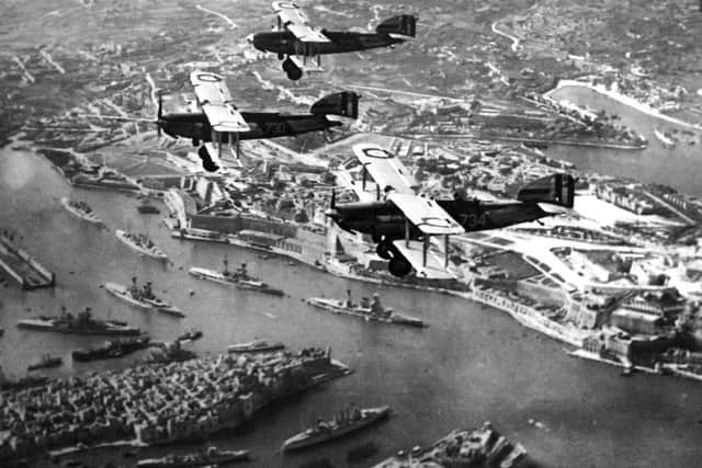 Three biplanes  over Malta . The picture was taken from a fourth. Below  is battleship row in Grand Harbour. Six battleships can be seen along with the floating dock (far left). A cruiser and destroyer are at the bottom.