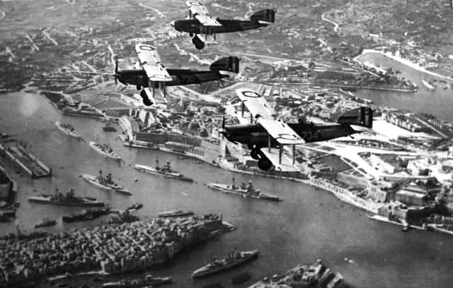 Three biplanes  over Malta . The picture was taken from a fourth. Below  is battleship row in Grand Harbour. Six battleships can be seen along with the floating dock (far left). A cruiser and destroyer are at the bottom.